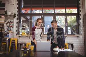 Man gesturing at laptop while standing by woman