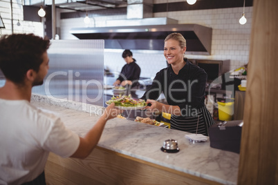 Smiling female chef giving fresh Greek salad to waiter