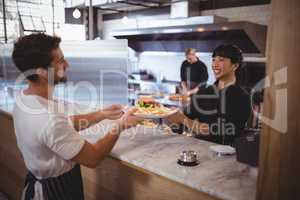Smiling young female chef giving burger and fries to waiter