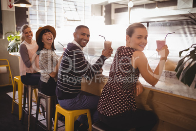 Portrait of smiling young friends holding drinks while sitting at counter