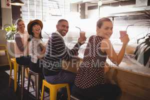 Portrait of smiling young friends holding drinks while sitting at counter