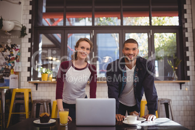 Portrait of smiling young man and woman standing at coffee shop