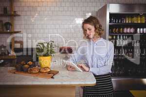 Attractive young waitress using digital tablet while standing by counter