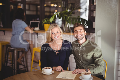 Smiling young couple sitting with coffee and menu at table in cafe