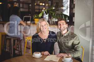 Smiling young couple sitting with coffee and menu at table in cafe
