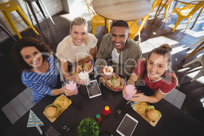 High angle portrait of smiling young friends sitting with lunch at coffee shop