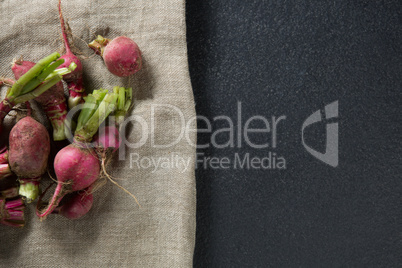 Overhead view of red radishes on burlap over slate