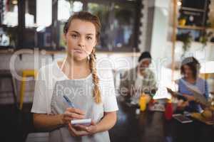 Confident young waitress standing with notepad at cafe