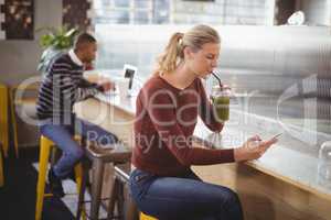 Young blond woman using smartphone while drinking juice at counter