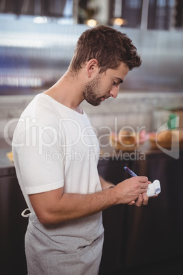 Side view of young handsome waiter writing in notepad at coffee shop