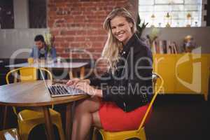 Portrait of smiling young woman sitting with laptop at coffee shop