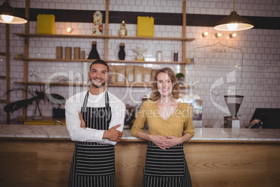 Portrait of smiling young wait staff standing against counter