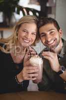 Smiling young couple holding fresh dessert at cafe