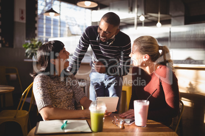 Cheerful man talking with female friends at coffee shop