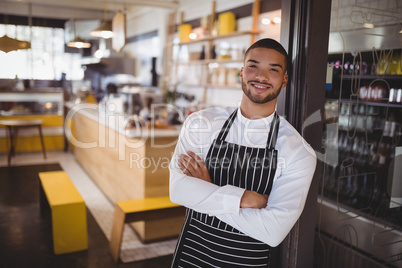 Portrait of smiling young handsome waiter with arms crossed leaning on cabinet
