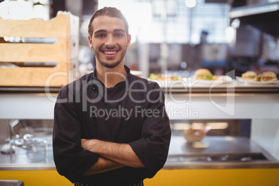 Portrait of smiling young waiter standing against counter