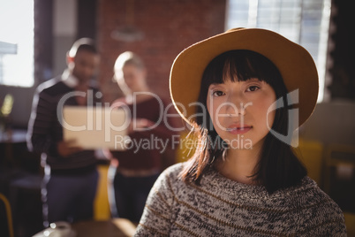 Portrait of confident young woman wearing hat while standing against colleagues