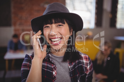 Cheerful young woman listening to mobile phone at coffee shop