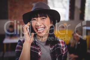 Cheerful young woman listening to mobile phone at coffee shop