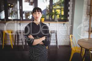 Portrait of confident young waitress standing with arms crossed