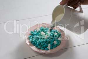Hand pouring milk into bowl of cereal rings and marsh mallow