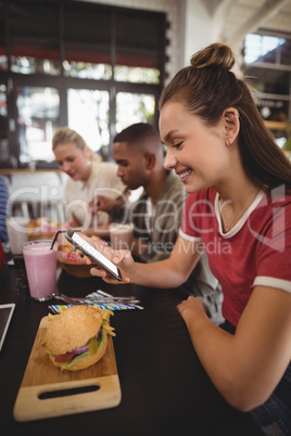 Side view of smiling young woman text messaging while sitting with burger