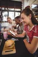 Side view of smiling young woman text messaging while sitting with burger