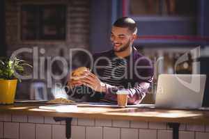 Smiling male professional holding fresh burger at coffee shop