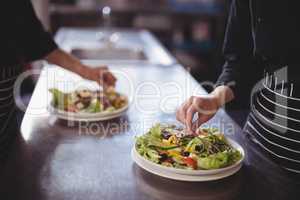 Midsection of waiter and waitress preparing fresh salad in commercial kitchen