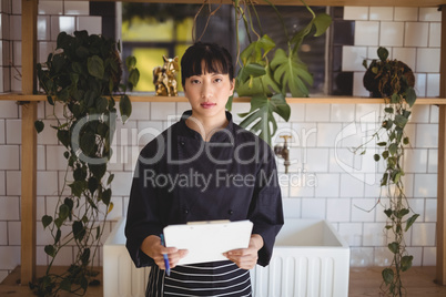 Portrait of young waitress holding clipboard against shelf