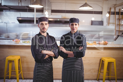 Portrait of confident young wait staff in black uniform standing with arms crossed at coffee shop