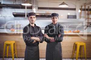 Portrait of confident young wait staff in black uniform standing with arms crossed at coffee shop