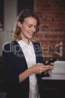 Smiling young beautiful female editor using smartphone at coffee shop