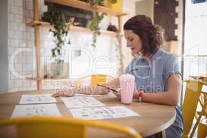 Young woman sitting with papers and drink at coffee shop