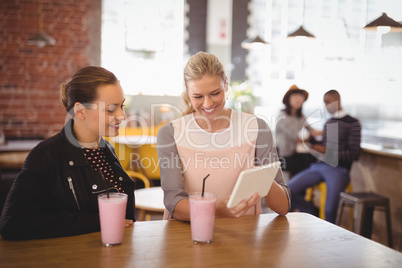 Smiling young female friends using tablet computer at coffee shop