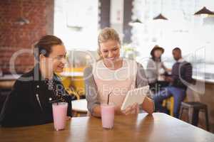 Smiling young female friends using tablet computer at coffee shop