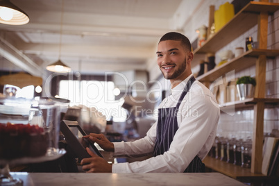 Smiling handsome young waiter using computer at counter