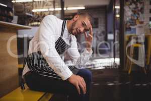 Upset young waiter sitting with headache while looking away