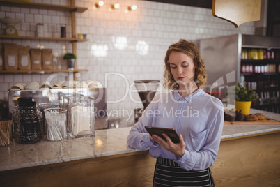 Young attractive waitress using digital tablet while standing by counter