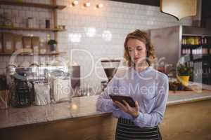Young attractive waitress using digital tablet while standing by counter