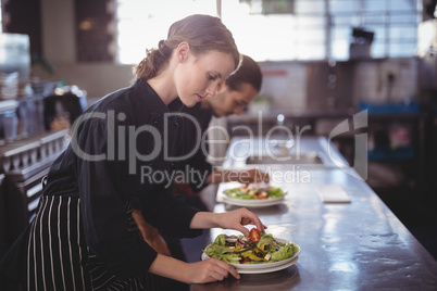 Side view of young wait staff preparing fresh salad plates while standing in commercial kitchen