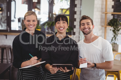 Portrait of smiling young wait staff holding digital tablet with notepad and clipboard