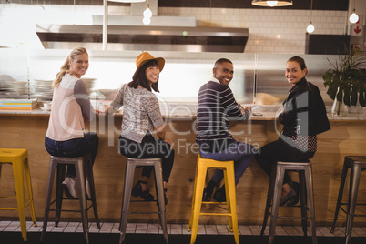 Rear view portrait of smiling young friends sitting on stools at counter