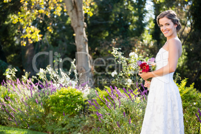 Portrait of smiling bride holding bouquet while standing on field