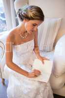 Beautiful bride writing in diary while sitting on armchair