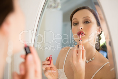 Side view of beautiful bride applying lip gloss reflecting on mirror