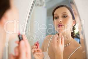 Side view of beautiful bride applying lip gloss reflecting on mirror