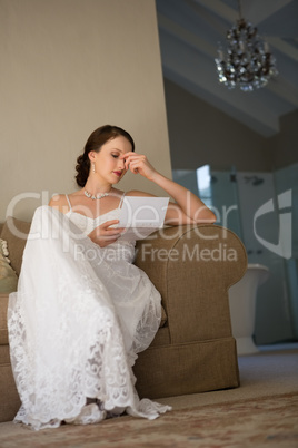 Low angle view of beautiful bride reading wedding card while sitting on sofa
