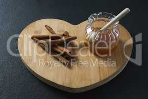 Cinnamon sticks and honey on heart shaped chopping board
