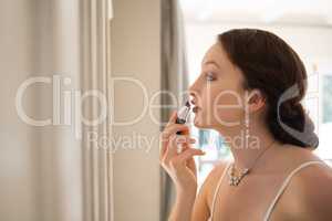 Beautiful bride applying lipstick while looking into mirror at home